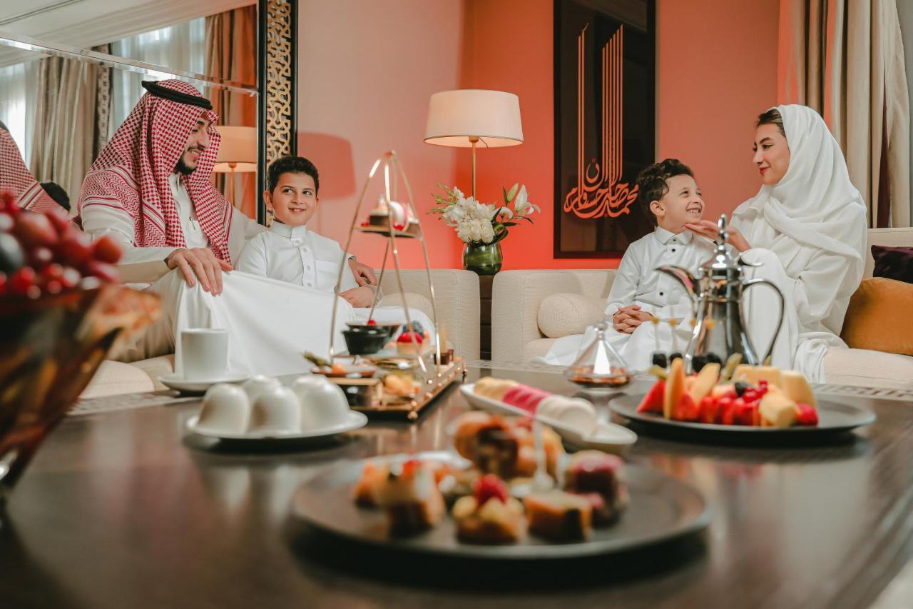 샤자 마디나 호텔 메디나 외부 사진 The photo depicts a cozy and inviting indoor setting where a family appears to be spending time together. In the foreground, there are plates of desserts and fruits arranged on a table, showcasing a variety of colorful treats. 

In the background, a 