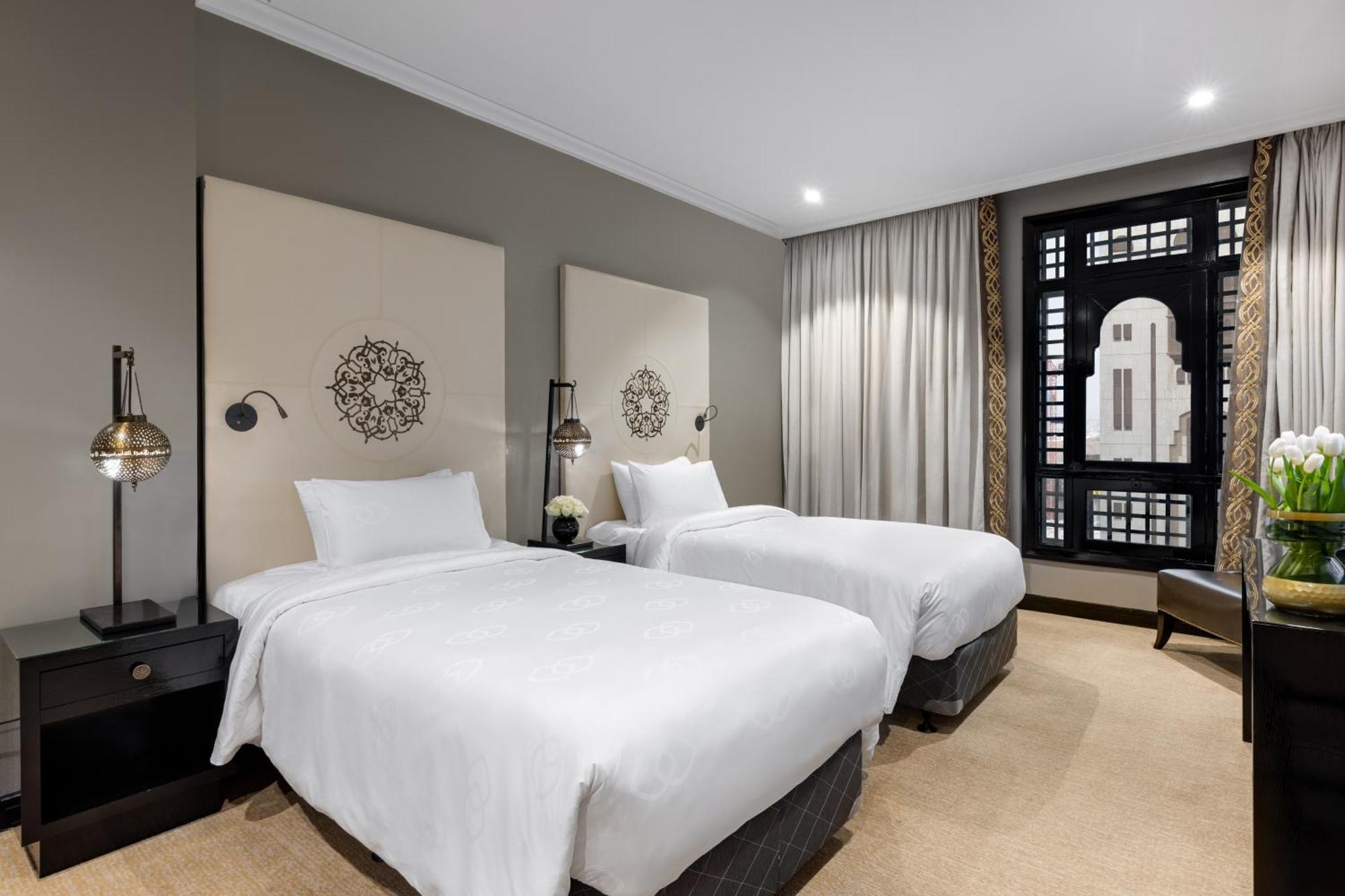 샤자 마디나 호텔 메디나 외부 사진 The photo shows a modern hotel room featuring two twin beds with white linens. Each bed is flanked by bedside tables with stylish lamps. The walls are painted in a neutral tone, and there are decorative panels behind the beds, adding a touch of elega