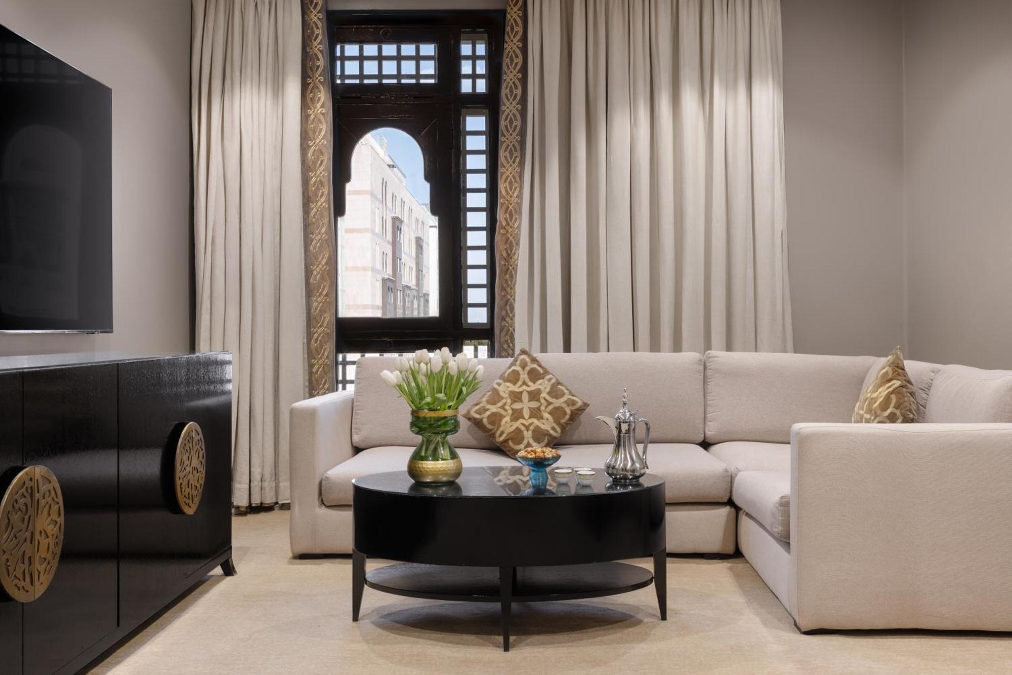 샤자 마디나 호텔 메디나 외부 사진 The photo shows a stylish and modern living room. It features a light-colored sectional sofa with decorative cushions, positioned around a round black coffee table. On the table, there’s a vase with flowers and some decorative items. The room has lar