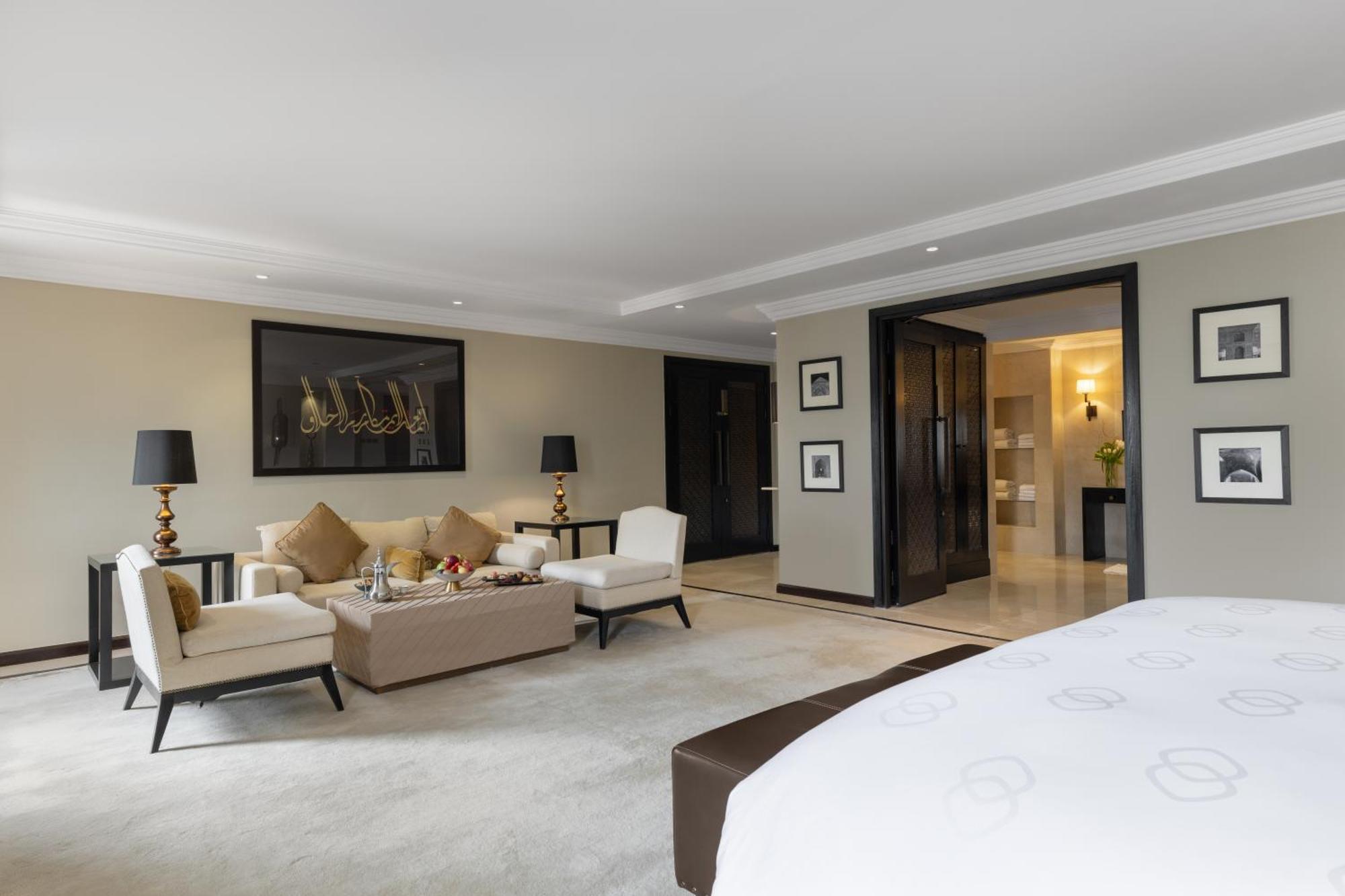 샤자 마디나 호텔 메디나 외부 사진 The photo depicts a spacious and elegantly designed hotel suite. In the foreground, there is a large bed with a dark headboard. To the right of the bed, there is a plush carpeted area. 

In the living area, there are two light-colored armchairs and a