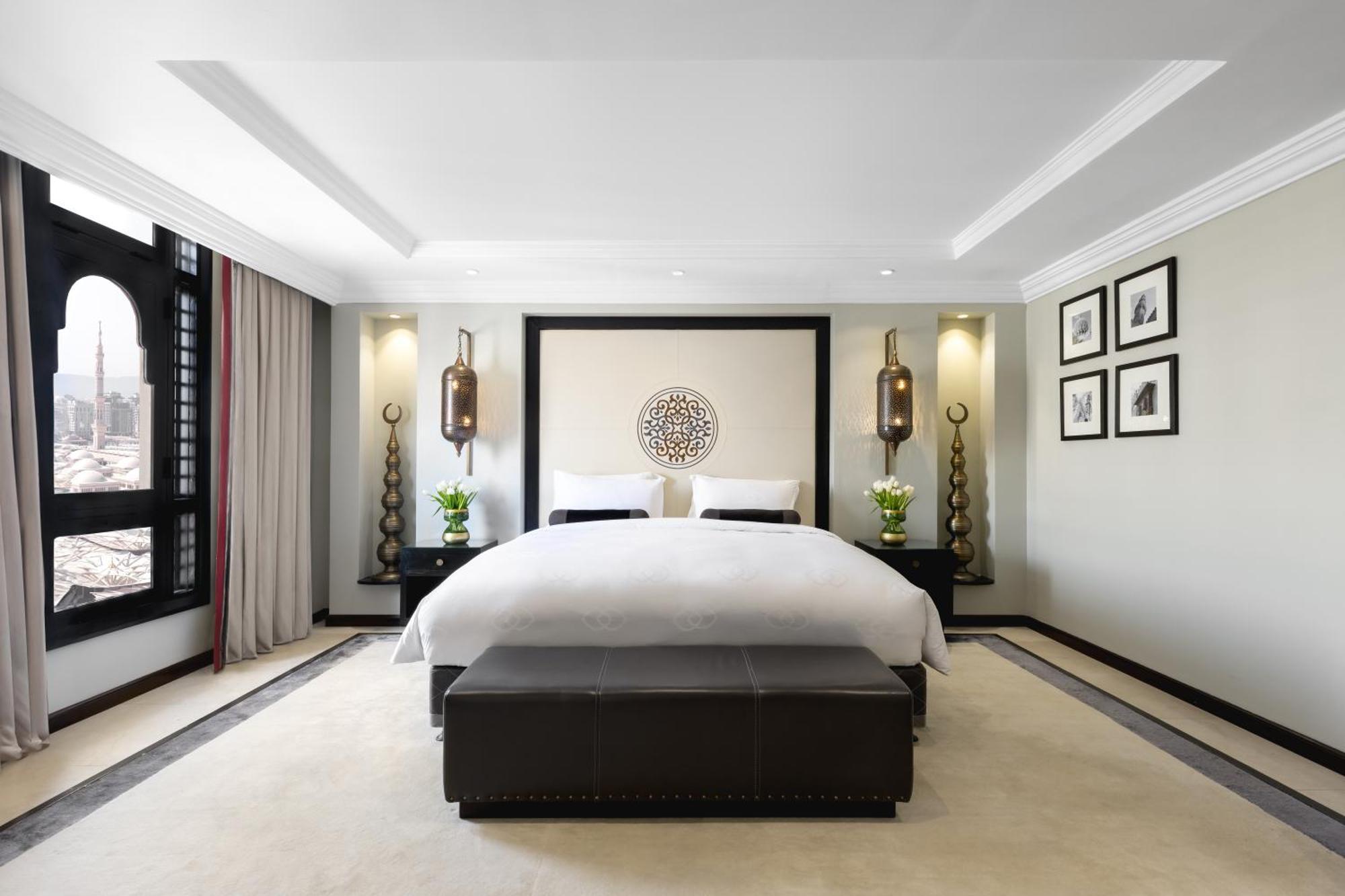 샤자 마디나 호텔 메디나 외부 사진 The photo shows a modern and stylish bedroom. It features a large bed with white linens, placed against a decorative wall with a circular design. On either side of the bed, there are elegant wall lamps illuminating the space. The room has a soft colo