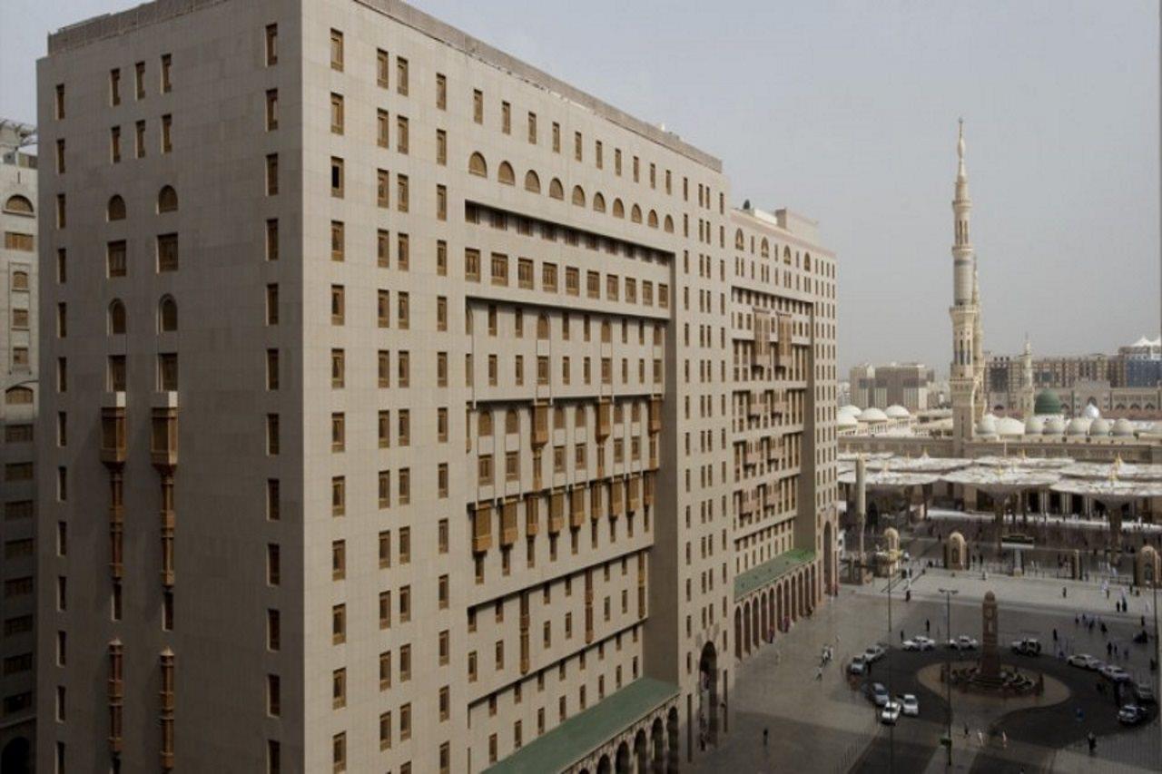 샤자 마디나 호텔 메디나 외부 사진 The photo shows a large modern building with a facade that features numerous windows and architectural detailing. It is situated in an urban setting, with another prominent structure, likely a mosque or minaret, visible in the background. The surroun